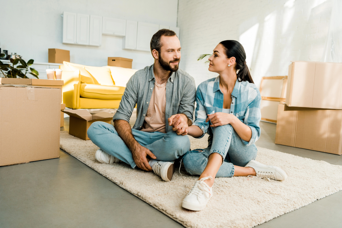 Husband and wife sitting on floor and holding hands while packing for new house Husband and wife sitting on floor and holding hands while packing for new house